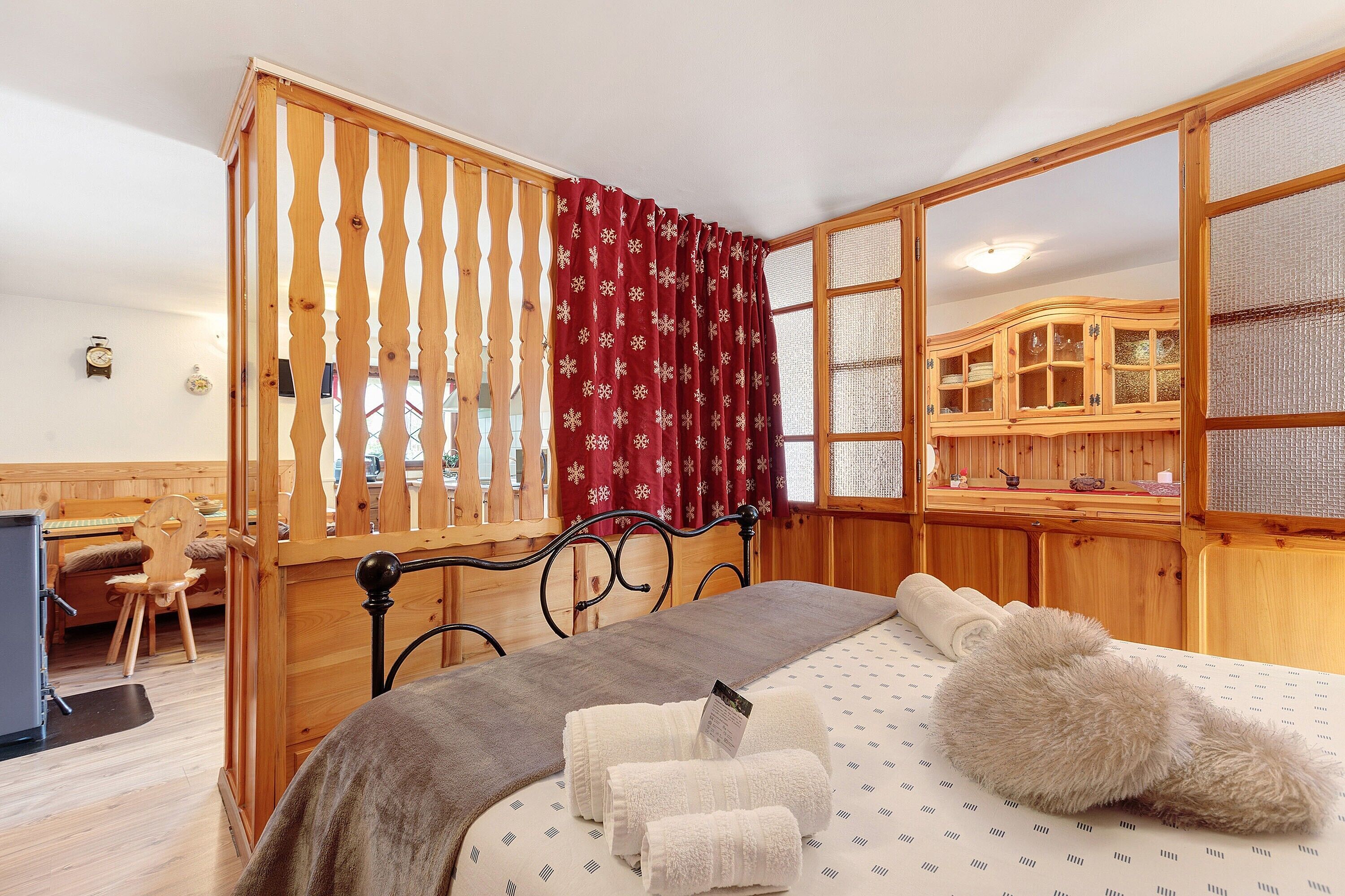 A room with a bed, wooden furniture, a desk, and a window with a red curtain.. Petit Logement Cerise "L'écrin d'Ari" – Comfort and Perfect Location