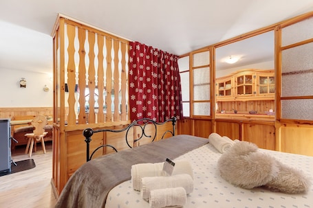 A room with a bed, wooden furniture, a desk, and a window with a red curtain.. Petit Logement Cerise "L'écrin d'Ari" – Comfort and Perfect Location