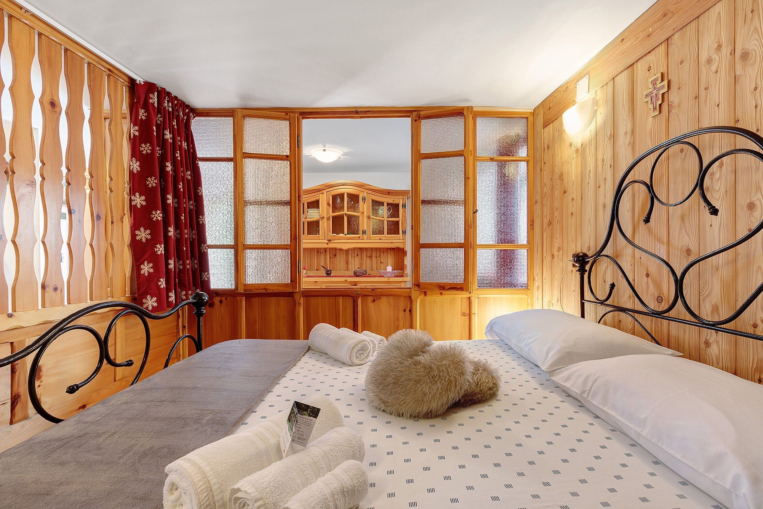 A wooden-paneled room with a bed, a wooden cabinet, and a window with red curtains.