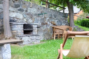 A stone wall, a stone fireplace, wicker furniture, and a wooden bench. - Petit Logement Cerise "L'écrin d'Ari" – Comfort and Perfect Location (La Cerise)