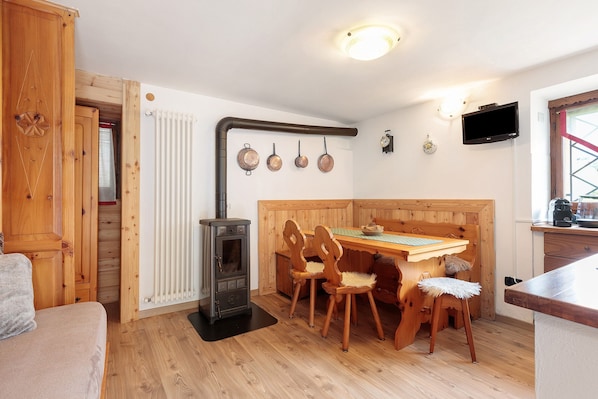 Une pièce chaleureuse avec une table à manger en bois, des chaises, un poêle et un téléviseur fixé au mur.