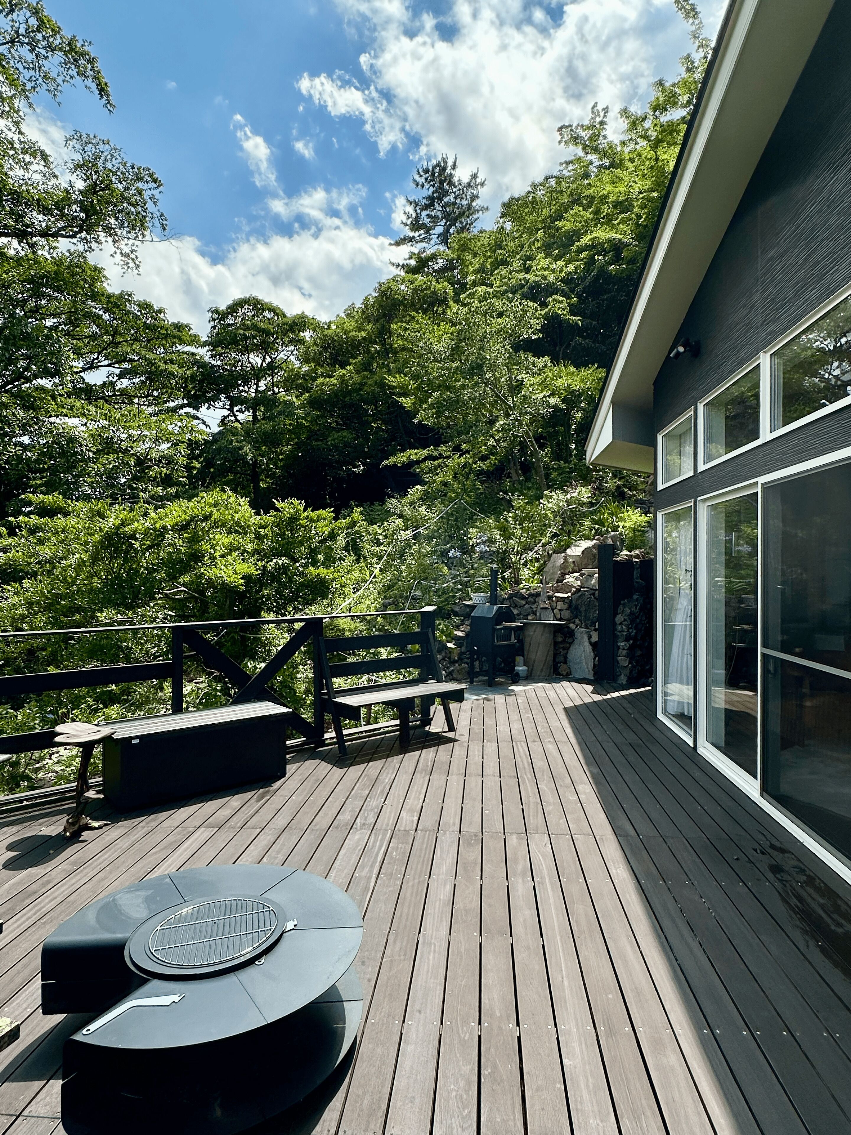 A wooden deck with a grill, benches, and a view of a forested area.