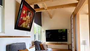 Uma sala de estar moderna com uma televisão de tela plana grande, dois sofás cinzas com almofadas, uma obra de arte emoldurada e piso de tatame.