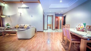 Un salon moderne comprenant un canapé, une table à manger et des chaises. On y trouve une petite table avec une lampe et une plante décorative. La pièce est dotée d’un parquet et d’un plafond avec des spots encastrés.