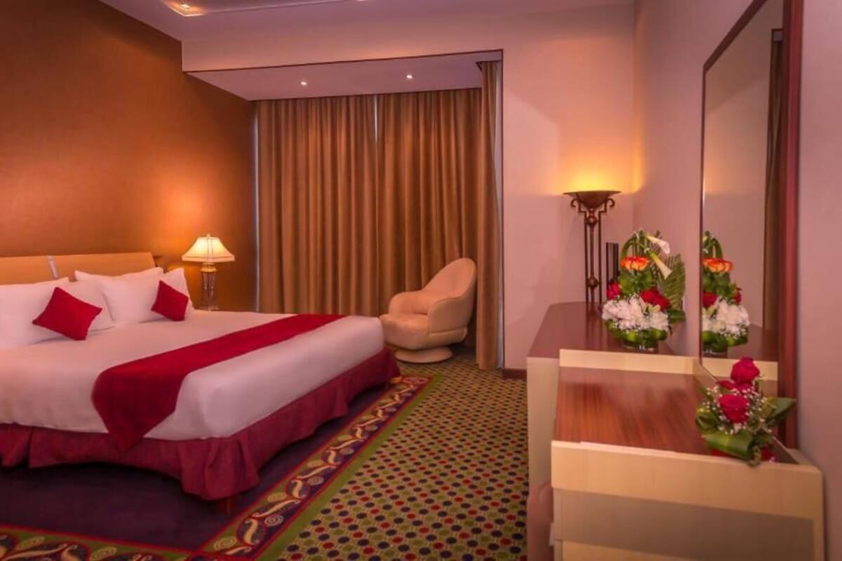 A hotel room with a large bed, a chair, a desk, and a mirror.