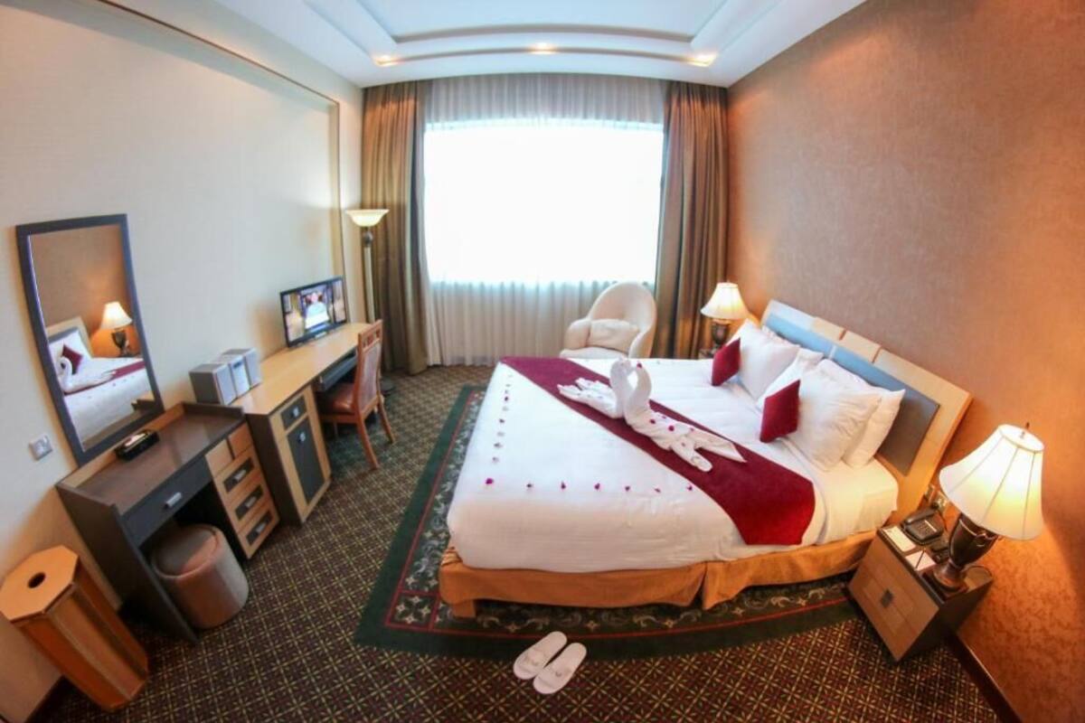 A hotel room with a bed, desk, chair, and a large window.