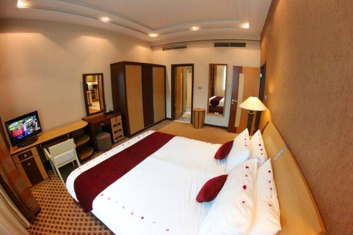 A hotel room with a bed, a desk, a television, a mirror, and a lamp.