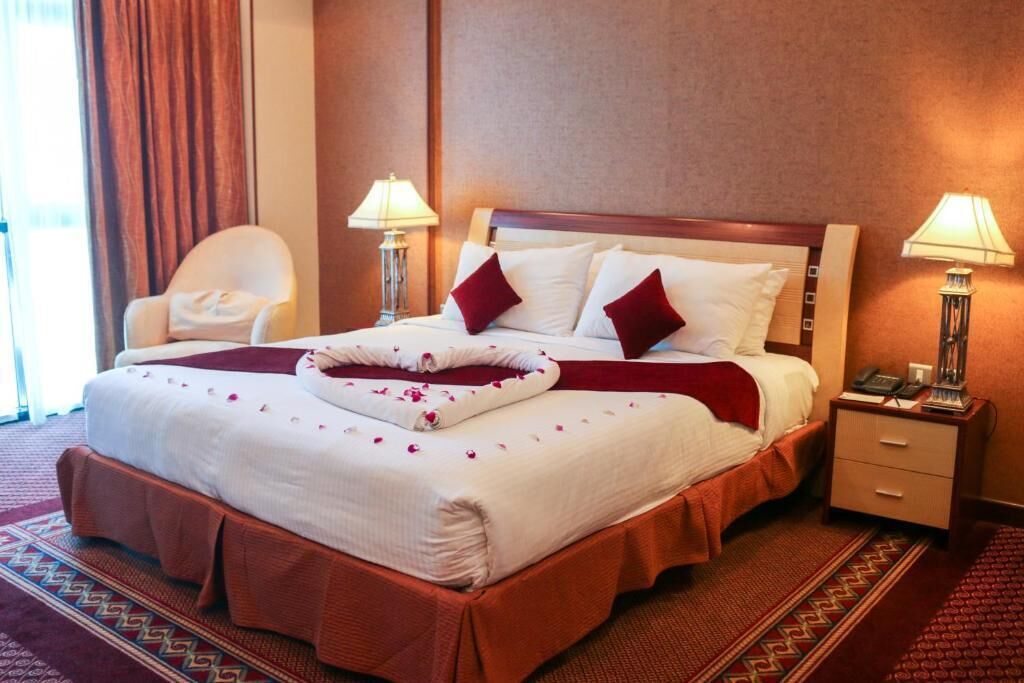 A hotel room with a large bed, two bedside tables, a chair, and a window with curtains.