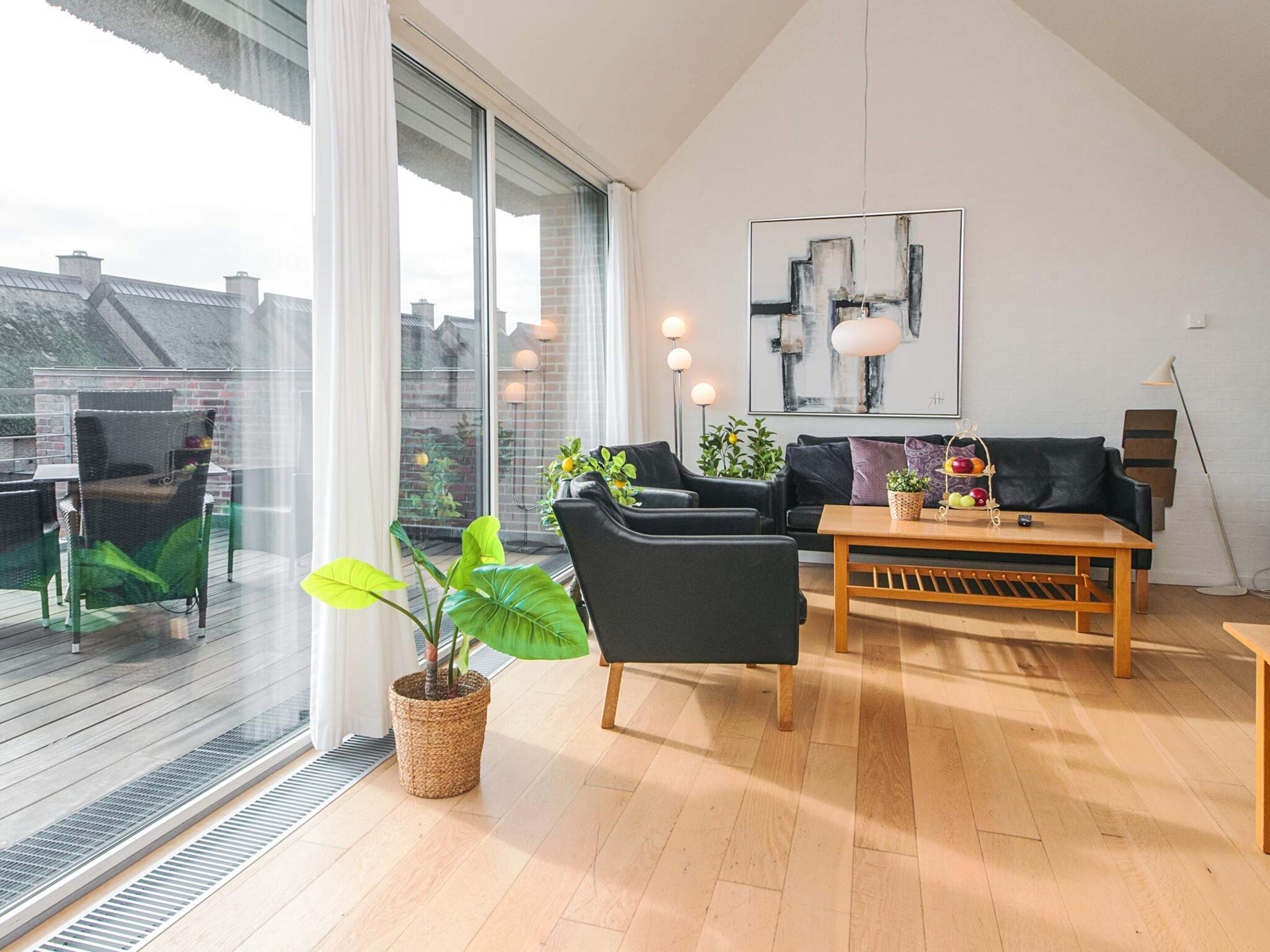 A modern living room with a large window, a black sofa, a wooden coffee table, and a potted plant.