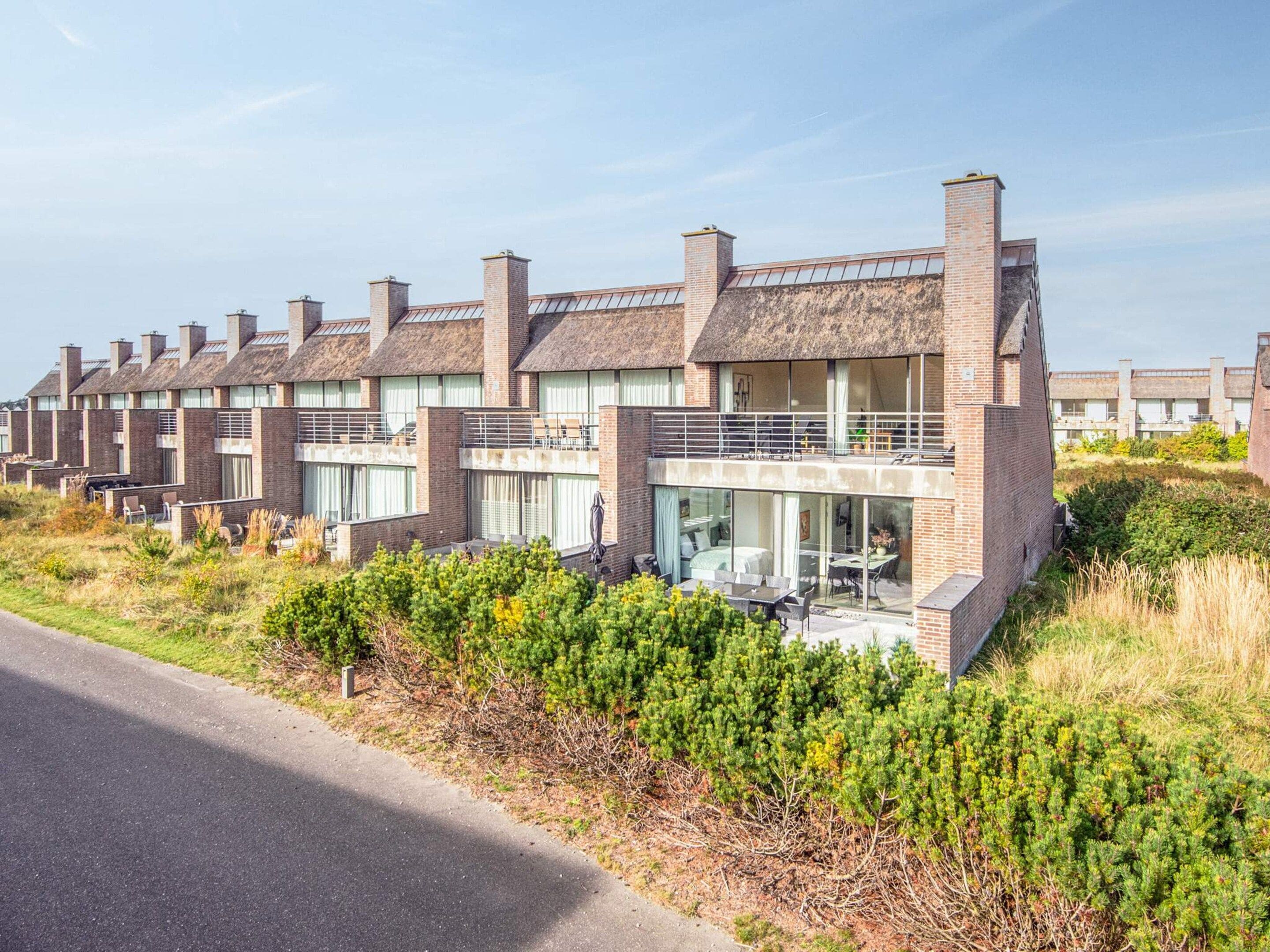 A row of modern brick houses with large windows and balconies, surrounded by greenery.