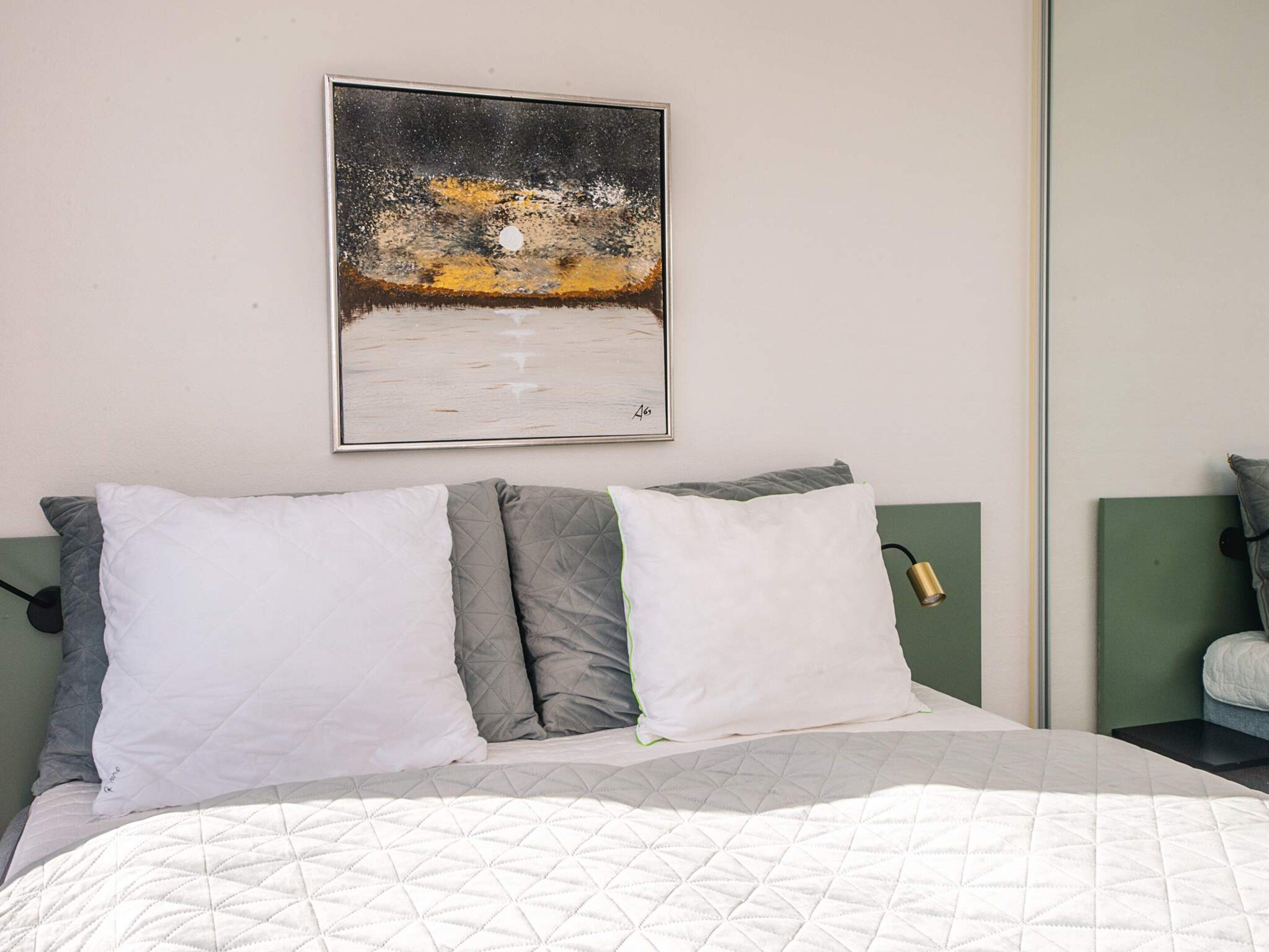 A bedroom with a bed, pillows, a nightstand, a lamp, and a painting on the wall.