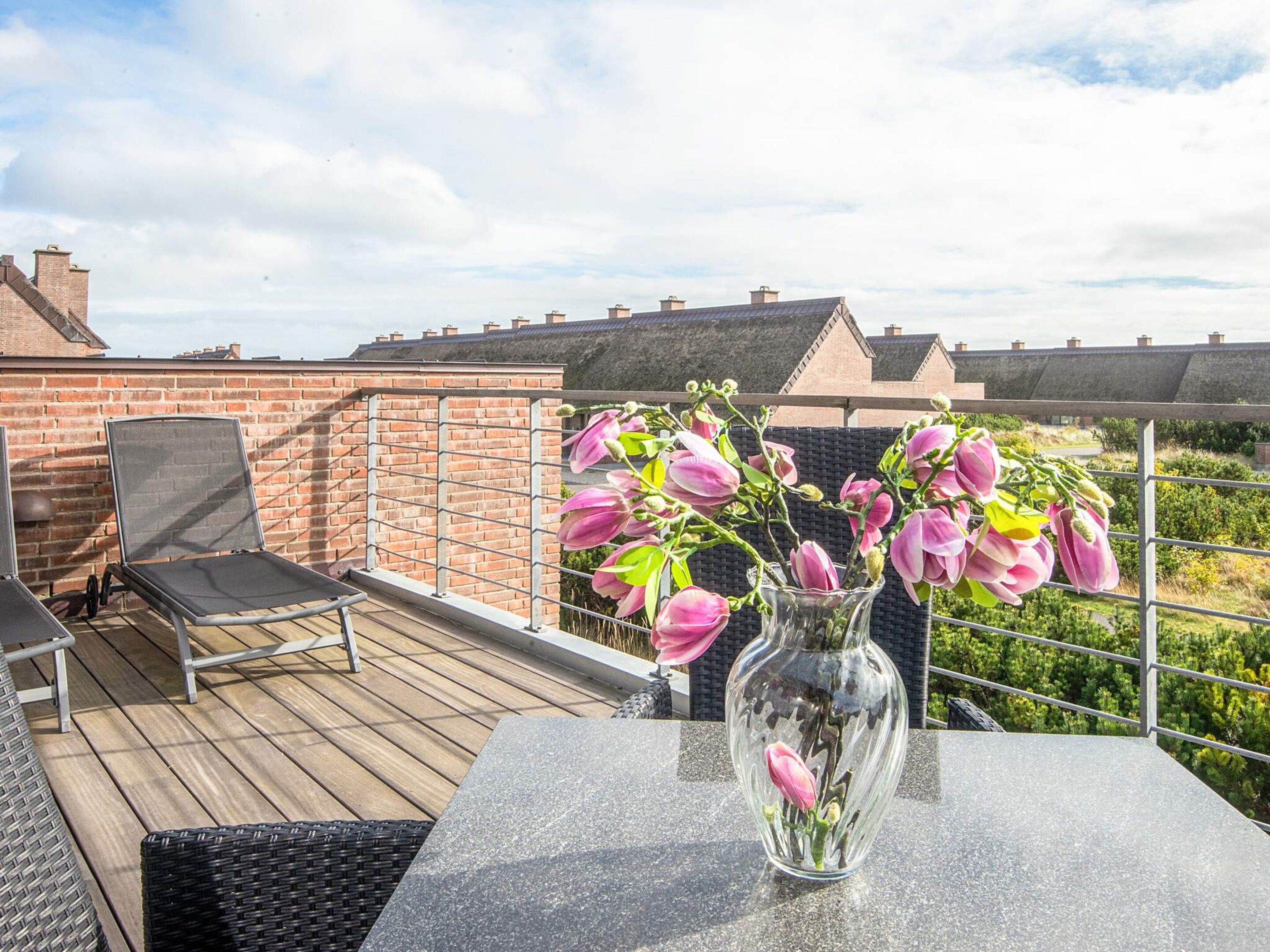 A rooftop terrace with a table, chairs, and a vase of flowers.