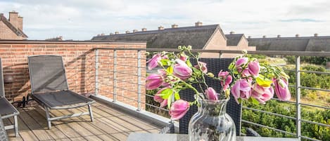 A rooftop terrace with a table, chairs, and a vase of flowers.