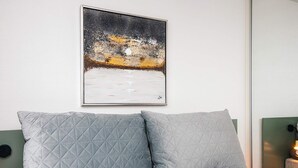 Ein Schlafzimmer mit einem Bett, zwei Kissen, einem gerahmten Bild an der Wand und einem Nachttisch mit einer Lampe.