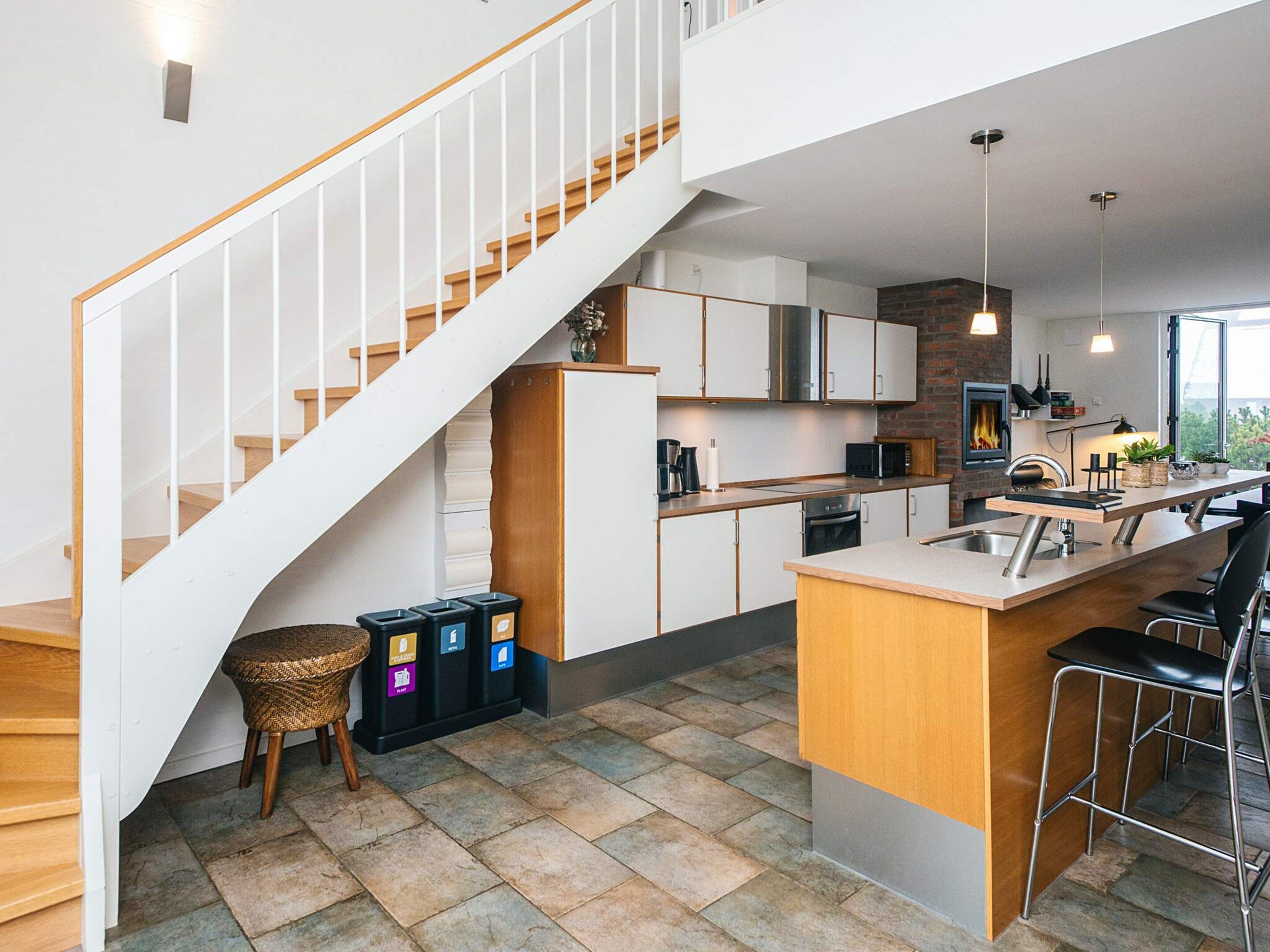 Una cocina moderna con una isla central, una escalera y un comedor con taburetes de bar.