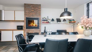 Ein moderner Essbereich mit Kamin aus Ziegelsteinen, schwarzen Ledersesseln, einem weißen Tisch und einem Blumenstrauß.