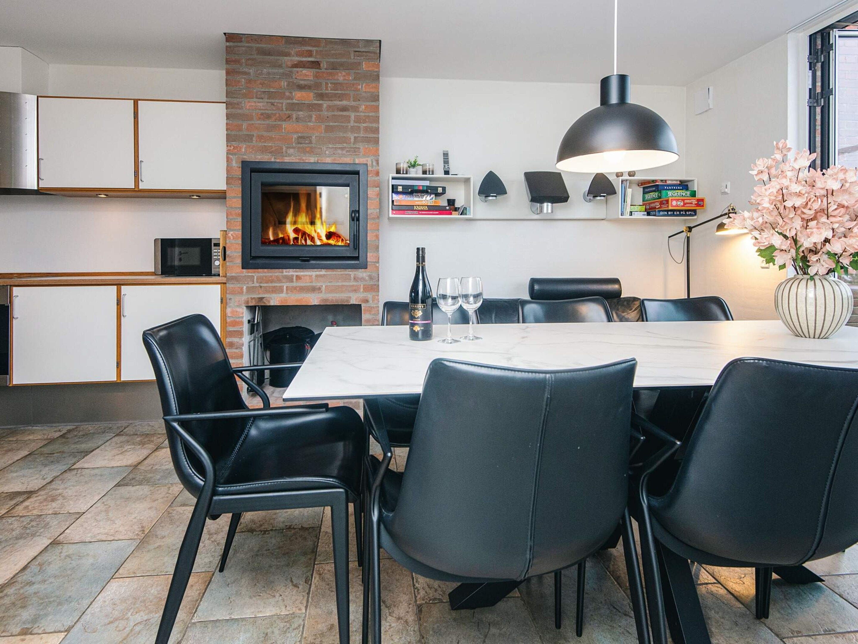Et moderne spiseområde med en murstenspejs, sorte læderstole, et marmorbord og en vase med blomster.