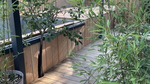 Eine Holzterrasse mit einem Blumentopf, ein Holzzaun und im Hintergrund ein Gebäude mit einem Ziegeldach.