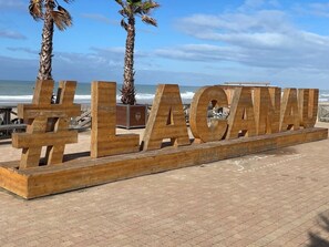 Ein Holzschild mit dem Schriftzug '#LACANNU' und Palmen im Hintergrund.