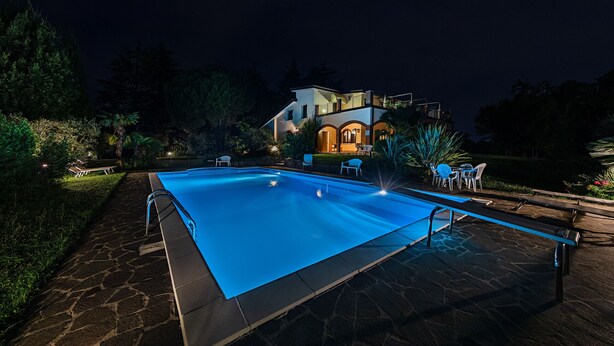 Une piscine avec une terrasse en pierre, entourée de meubles d’extérieur et d’une maison dotée d’un balcon.