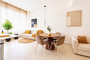 A modern living room with a round dining table, sofas, and a large window with curtains. - DomusNova Zaffiro - Suite historic center Turin (Torino)