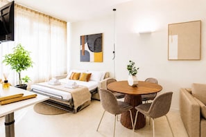 A modern hotel room with a bed, bedside table, a round wooden dining table with chairs, a sofa, a large mirror, and a painting on the wall. - DomusNova Zaffiro - Suite historic center Turin (Torino)