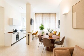 A modern kitchen with white cabinets, a dining area with a round table and chairs, and a living room with a sofa and a plant. - DomusNova Zaffiro - Suite historic center Turin (Torino)