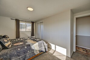 A bedroom with a bed, a window with curtains, a door, and a carpeted floor.