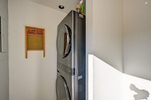 A laundry area with a stainless steel washer and dryer, a wooden sign on the wall, and a white wall.