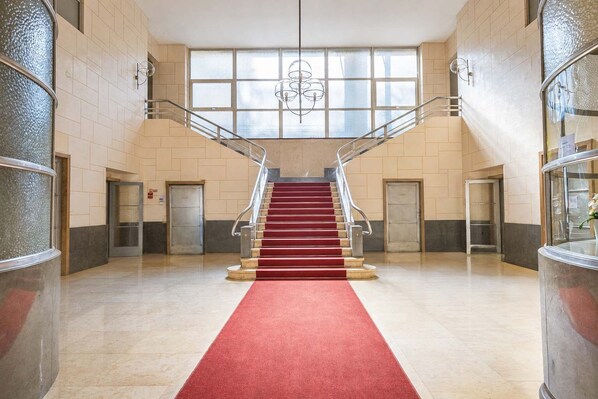 Eine prächtige Treppe mit rotem Teppich, der zu einer oberen Etage führt, gesäumt von Glasüren und einer modernen Leuchte.