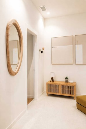 A hallway with a wooden mirror, a wooden console table with a lamp, and two framed artworks on the wall. - DomusNova Rubino | Suite historic center Turin (Torino)
