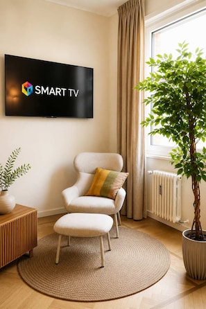 Ein modernes Wohnzimmer mit Flachbildfernseher, einem bequemen Sessel, einem kleinen Tisch, einem Blumentopf und einer Heizung.