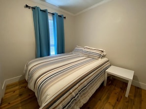 Quarto com cama, mesa de cabeceira e janela com cortinas.