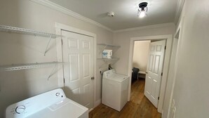 A laundry room with a front-loading washer and dryer, shelving above the washer, and a door leading to another room. - Off Main Downtown BV Cottage - STR-048 (Buena Vista)