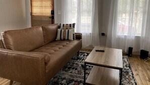 A living room with a brown leather sofa, a wooden coffee table, and a patterned rug. - Off Main Downtown BV Cottage - STR-048 (Buena Vista)