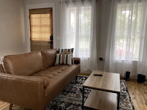 Uma sala de estar com um sofá de couro marrom, uma mesa de centro de madeira e um tapete estampado.