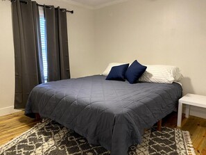 Een slaapkamer met een bed, nachtkastje, raam met gordijnen en een kamerbreed tapijt.