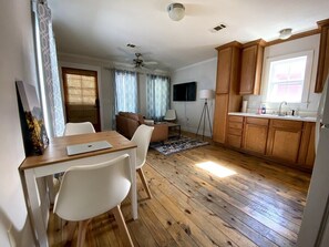 A compact living space with a dining area, a sofa, a TV, and a kitchen area. - Off Main Downtown BV Cottage - STR-048 (Buena Vista)