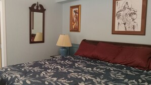 Un dormitorio con cama, mesita de noche, lámpara, espejo y obras de arte en las paredes.