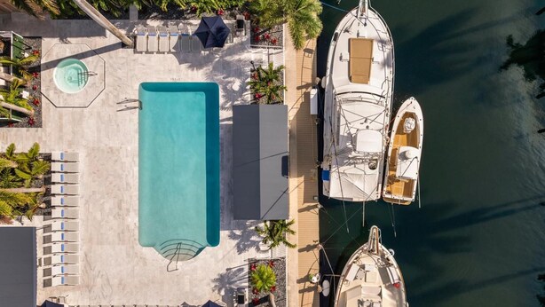 An aerial view of a resort with a large rectangular pool, several lounge chairs, and two boats docked at the marina.