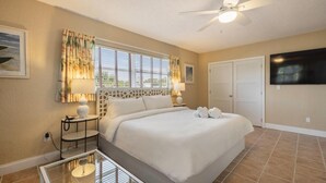 A hotel room with a large bed, a ceiling fan, a TV mounted on the wall, and a window with curtains.