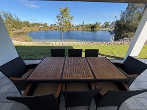 Une terrasse extérieure avec une table et des chaises en bois, donnant sur un lac et une végétation luxuriante.