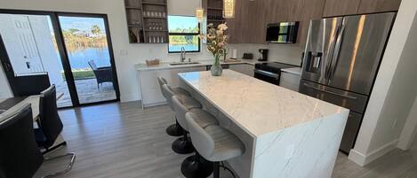 A modern kitchen with a large island, stainless steel appliances, and a view of a pool.