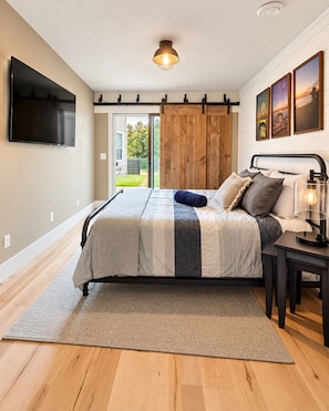 A bedroom with a bed, a TV, a wooden door, and artwork on the wall.