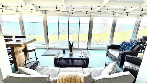 A room with a large window overlooking a body of water, furnished with a sofa, a coffee table, and a dining table.