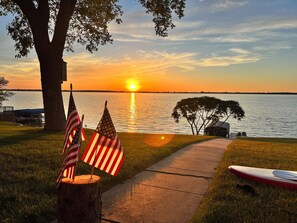 A sunset view over a lake with American flags, a kayak, and a tent.
