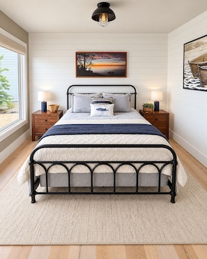 A bedroom with a bed, two bedside tables, a nightstand, a window, and a wall-mounted picture.