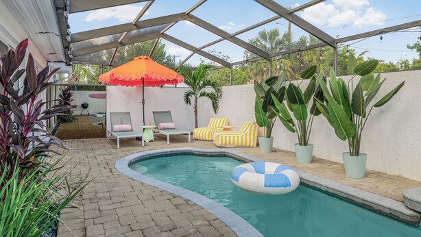 A covered outdoor pool area with lounge chairs, a small table, and potted plants. - Art Deco Den - Charming 3 bedroom home with pool in Tampa (Tampa)