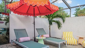 A poolside area with lounge chairs, a table with drinks, and a large umbrella. - Art Deco Den - Charming 3 bedroom home with pool in Tampa (Tampa)