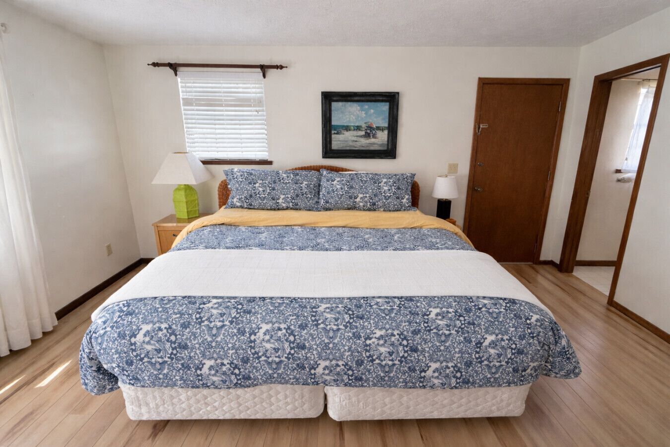 Un dormitorio con cama, un cuadro, una puerta y una ventana con persianas.